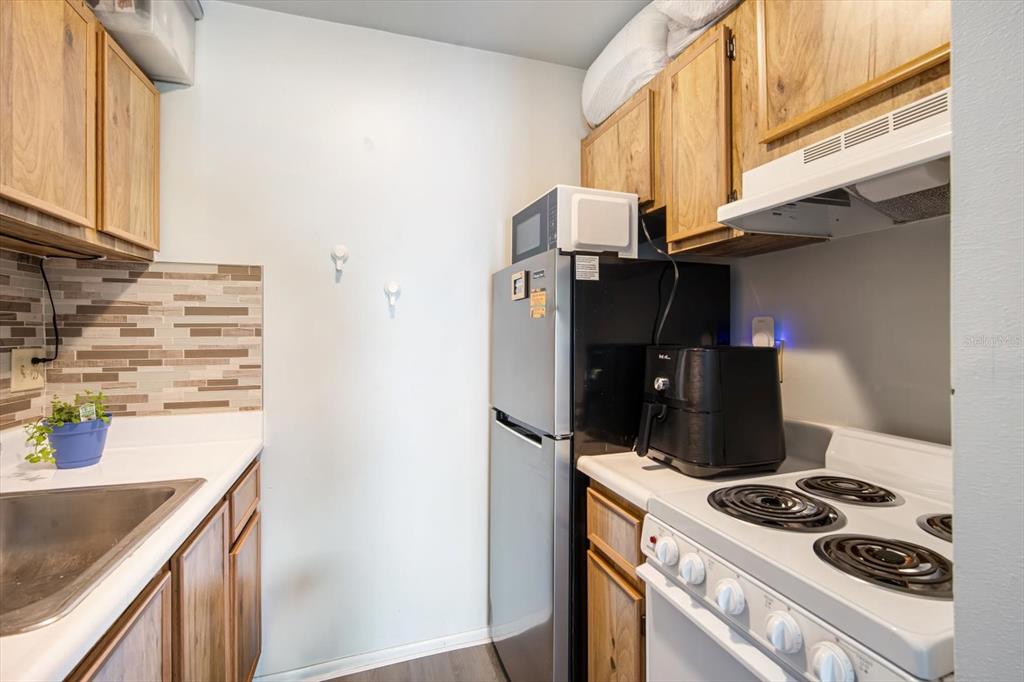 A small kitchen features wood cabinets, a stainless steel refrigerator, and a white electric stove — 4130 DOLPHIN DRIVE UNIT 203, TAMPA, FL