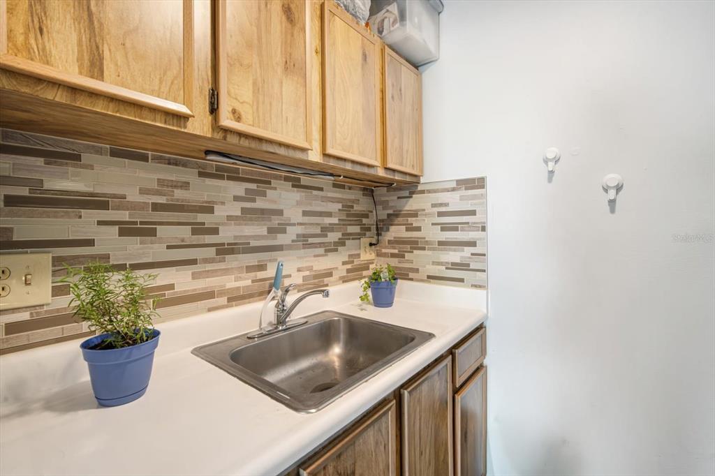 A laundry room sink features wood cabinets, a tiled backsplash, and a white countertop — 4130 DOLPHIN DRIVE UNIT 203, TAMPA, FL