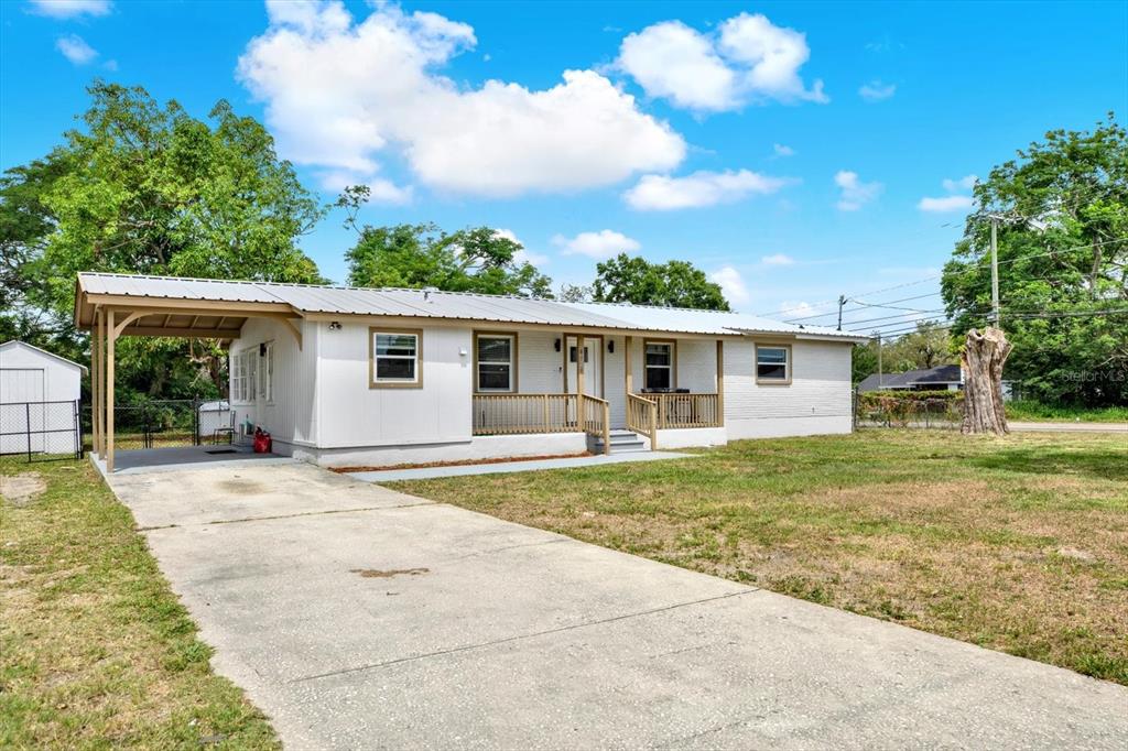 A white single-story house with a metal roof, carport, and wooden porch under a blue sky — 6020 N 50TH STREET, TAMPA, FL