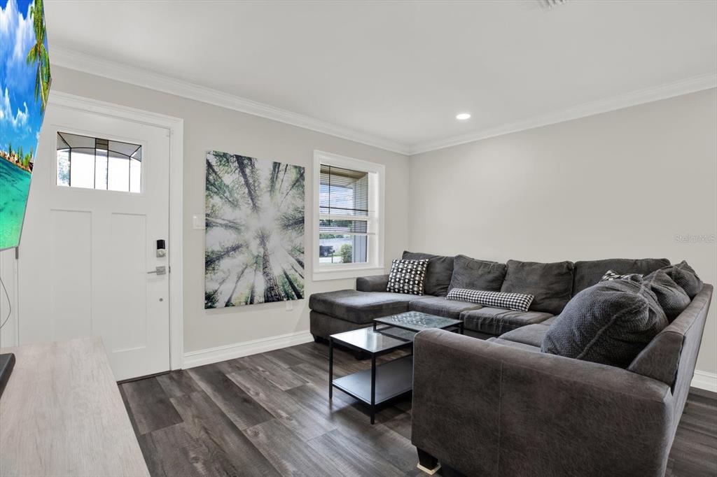 A living room features gray wood-look flooring, a dark sectional sofa, and a front door — 6020 N 50TH STREET, TAMPA, FL