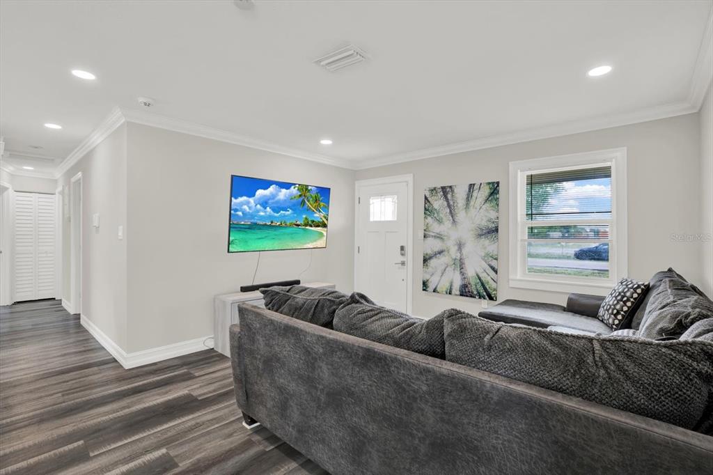 A living room features gray wood-look flooring, a sectional sofa, a wall-mounted television, and a window — 6020 N 50TH STREET, TAMPA, FL