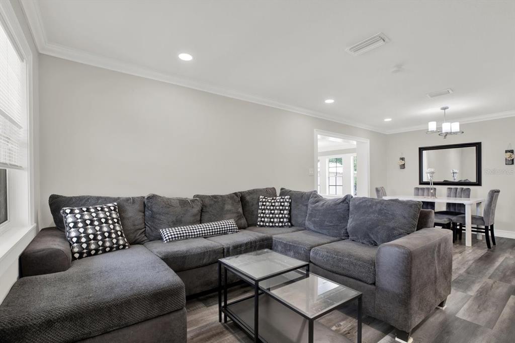 A living room features a large gray sectional sofa, two glass coffee tables, and wood-look flooring — 6020 N 50TH STREET, TAMPA, FL