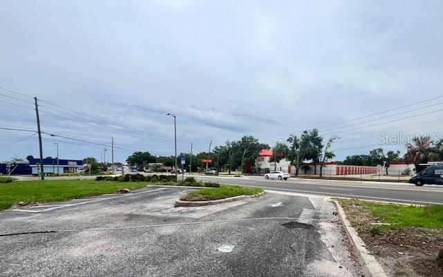 An asphalt parking lot sits in the foreground with a road and commercial buildings beyond — 101 W MAIN STREET, APOPKA, FL