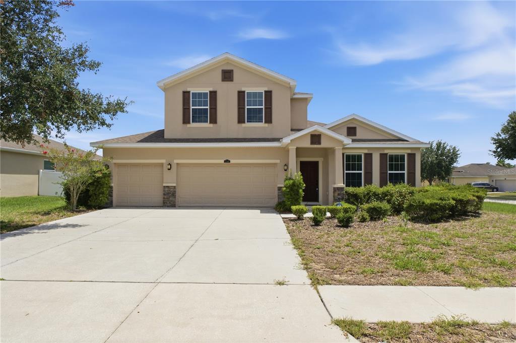 A two-story suburban house with a tan stucco exterior, brown shutters, and a three-car garage — 13366 BARKINGSIDE PLACE, SPRING HILL, FL