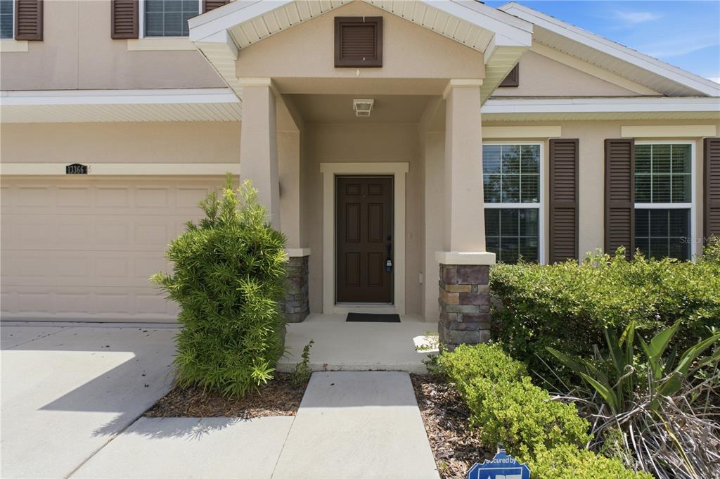 The exterior of a house features a tan facade, a brown front door, and stone accents — 13366 BARKINGSIDE PLACE, SPRING HILL, FL