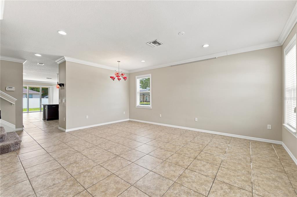 An open-concept living area features beige tile flooring, neutral walls, and a modern red chandelier — 13366 BARKINGSIDE PLACE, SPRING HILL, FL
