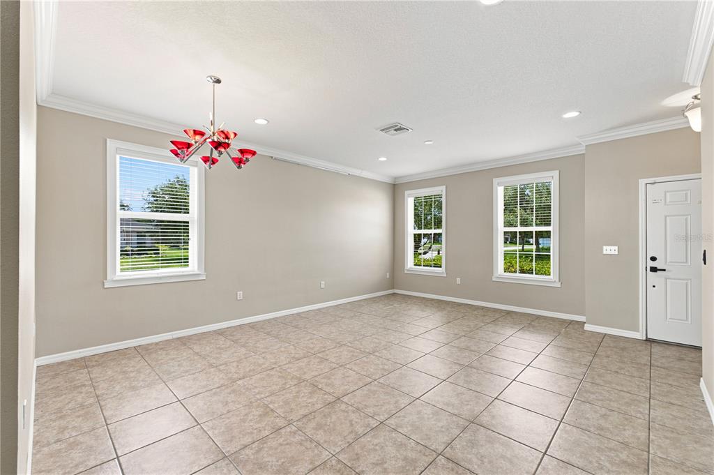 An empty room with beige walls, tile flooring, three windows, and a red chandelier — 13366 BARKINGSIDE PLACE, SPRING HILL, FL
