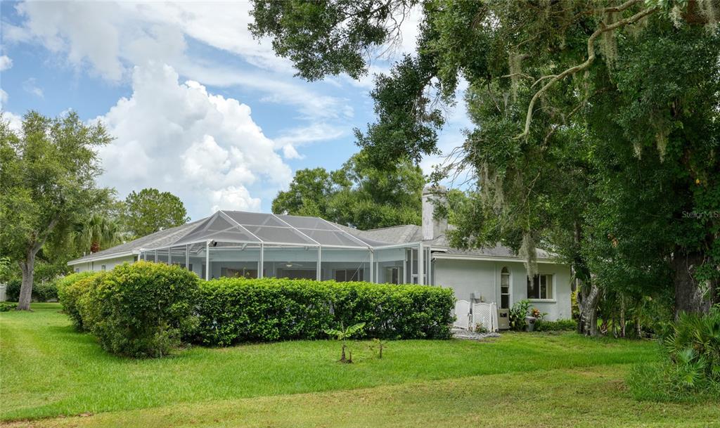 A backyard view of a house with a screened-in pool enclosure and surrounding green landscaping — 16215 HOYLAKE DRIVE, ODESSA, FL