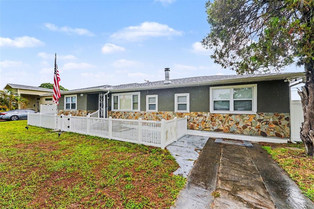 A single-story house with a stone facade, white picket fence, and an American flag — 6242 5TH AVENUE N, ST PETERSBURG, FL