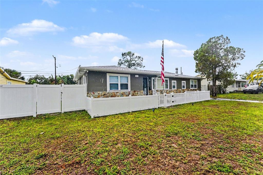 A single-story house with stone siding and a white fence sits on a grassy lot — 6242 5TH AVENUE N, ST PETERSBURG, FL