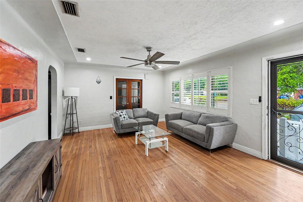 A living room features hardwood floors, two gray sofas, a glass coffee table, and shutters — 6242 5TH AVENUE N, ST PETERSBURG, FL