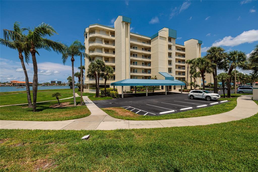 A multi-story beige apartment building with a covered parking area and palm trees — 7862 SAILBOAT KEY BOULEVARD S UNIT 506, SOUTH PASADENA, FL