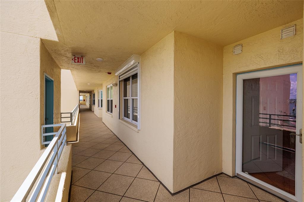 An outdoor apartment building walkway with beige stucco walls, tiled floors, and metal railings — 7862 SAILBOAT KEY BOULEVARD S UNIT 506, SOUTH PASADENA, FL