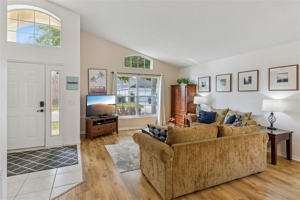 A living room with wood-look flooring, a tan sofa, and a television on a stand — 3062 BARBADOS LANE, HAINES CITY, FL
