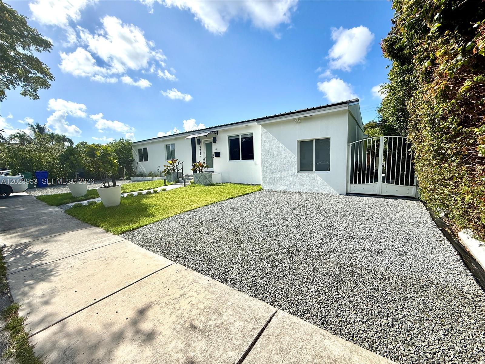 A white single-story house features a gravel driveway, a small lawn, and a gated entrance — 3280 SW 16th Ter, Miami FL 33145, MIAMI, FL
