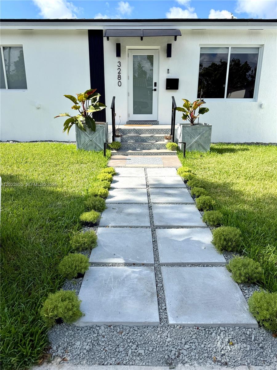 A white house exterior features a modern glass front door, concrete walkway, and potted plants — 3280 SW 16th Ter, Miami FL 33145, MIAMI, FL