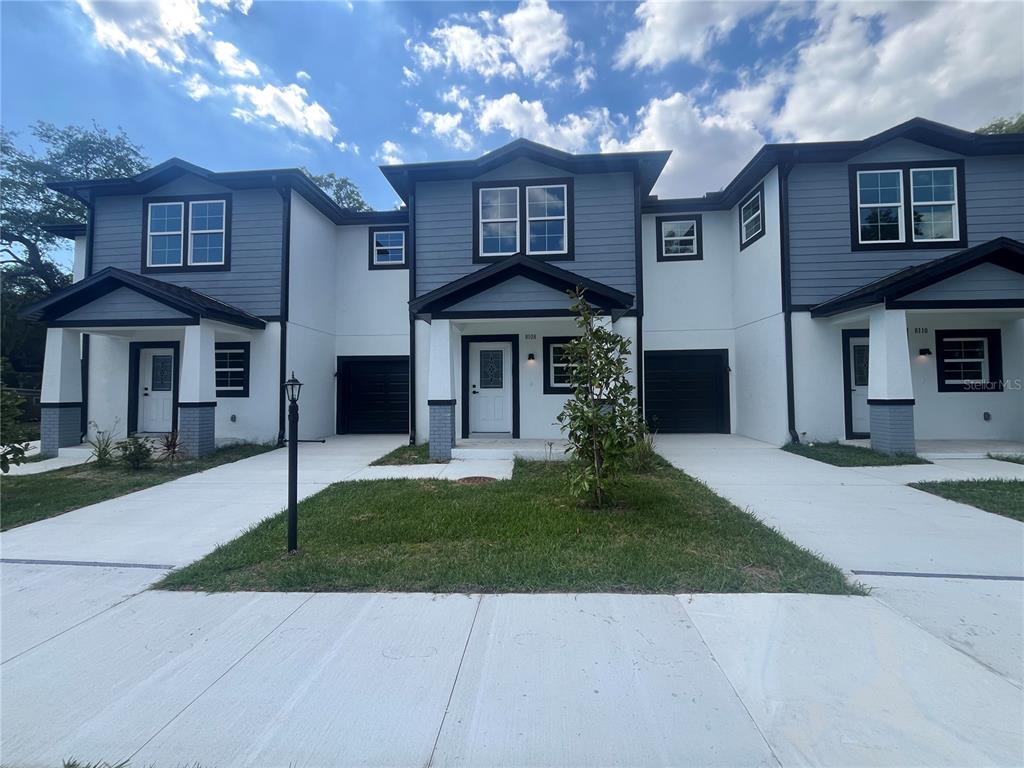 A three-unit townhouse building with white stucco, blue siding, and individual concrete driveways — 8108 N GREENWOOD AVENUE, TAMPA, FL