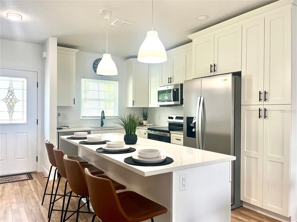 A modern kitchen features white cabinetry, a large island with bar seating, and stainless appliances — 8108 N GREENWOOD AVENUE, TAMPA, FL