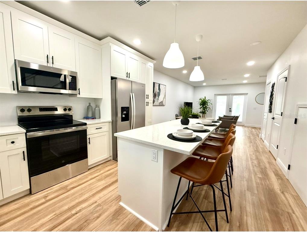 A modern kitchen features white cabinetry, stainless steel appliances, and a large island with seating — 8108 N GREENWOOD AVENUE, TAMPA, FL