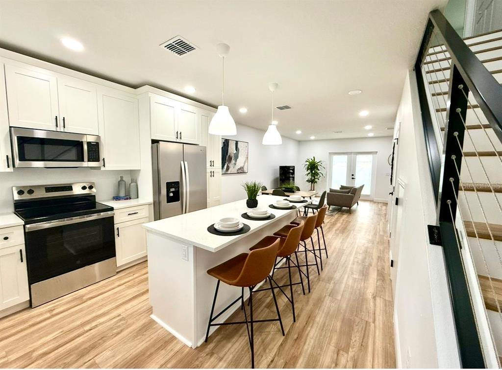 A modern kitchen features white cabinetry, stainless steel appliances, a central island, and wood flooring — 8108 N GREENWOOD AVENUE, TAMPA, FL