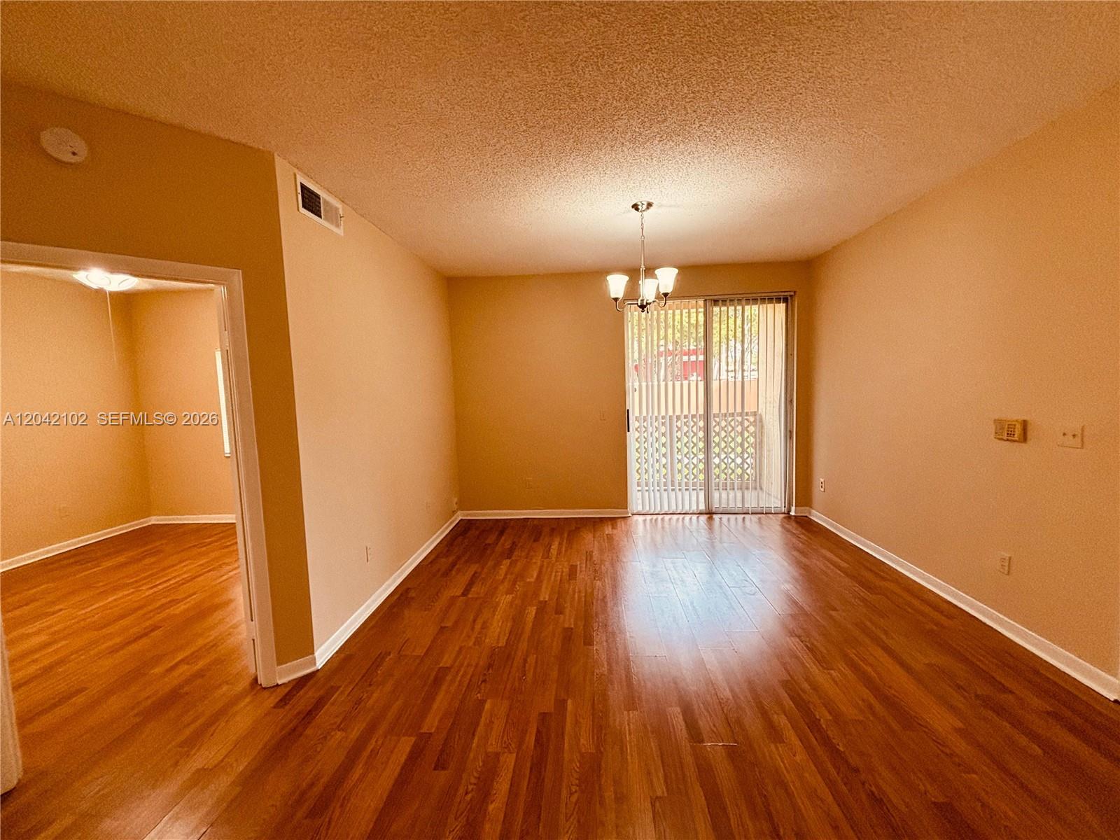 An empty living room features wood-look flooring, a chandelier, and sliding glass doors — HIALEAH, FL