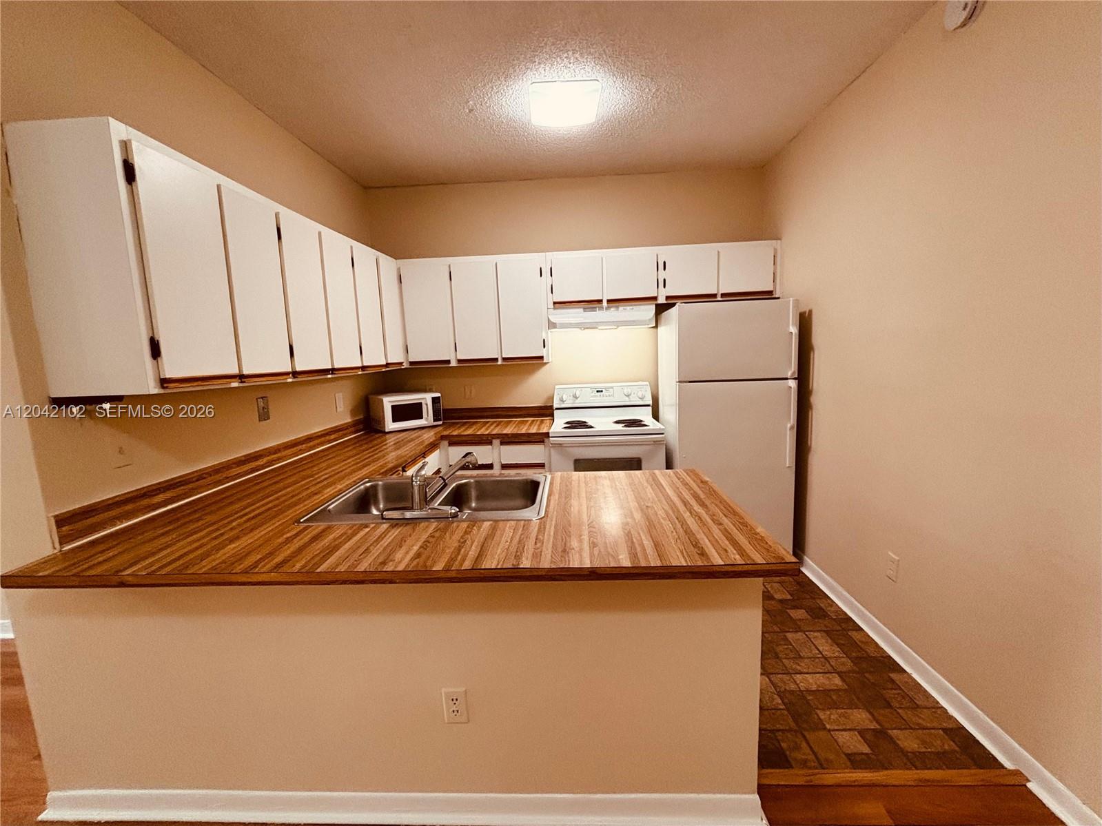 A kitchen features white cabinetry, wood-look laminate countertops, a double sink, and white appliances — HIALEAH, FL