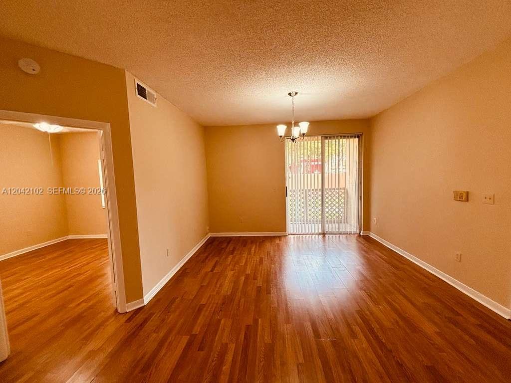 An empty room with wood-look flooring, a chandelier, and a sliding glass door — HIALEAH, FL