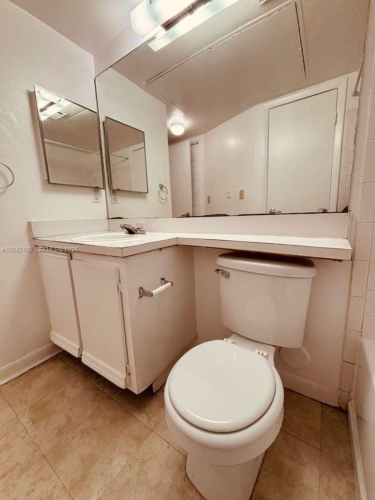 A bathroom features a white vanity, a toilet, and a large wall-mounted mirror — HIALEAH, FL