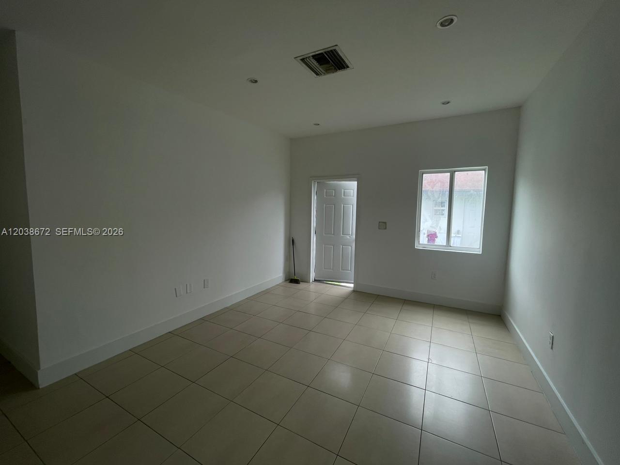 An empty room features white walls, light-colored tile flooring, a window, and a door — 4729 NW 15th Ave # 4727, Miami FL 33142, MIAMI, FL