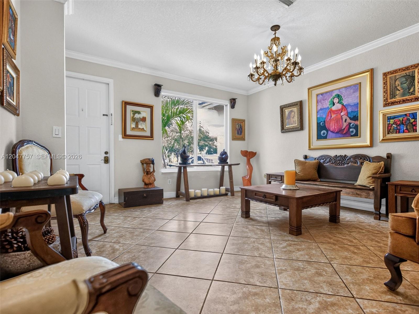 A living room features tile flooring, a chandelier, wooden furniture, and several framed paintings — 18843 SW 26th St, Miramar FL 33029, MIRAMAR, FL
