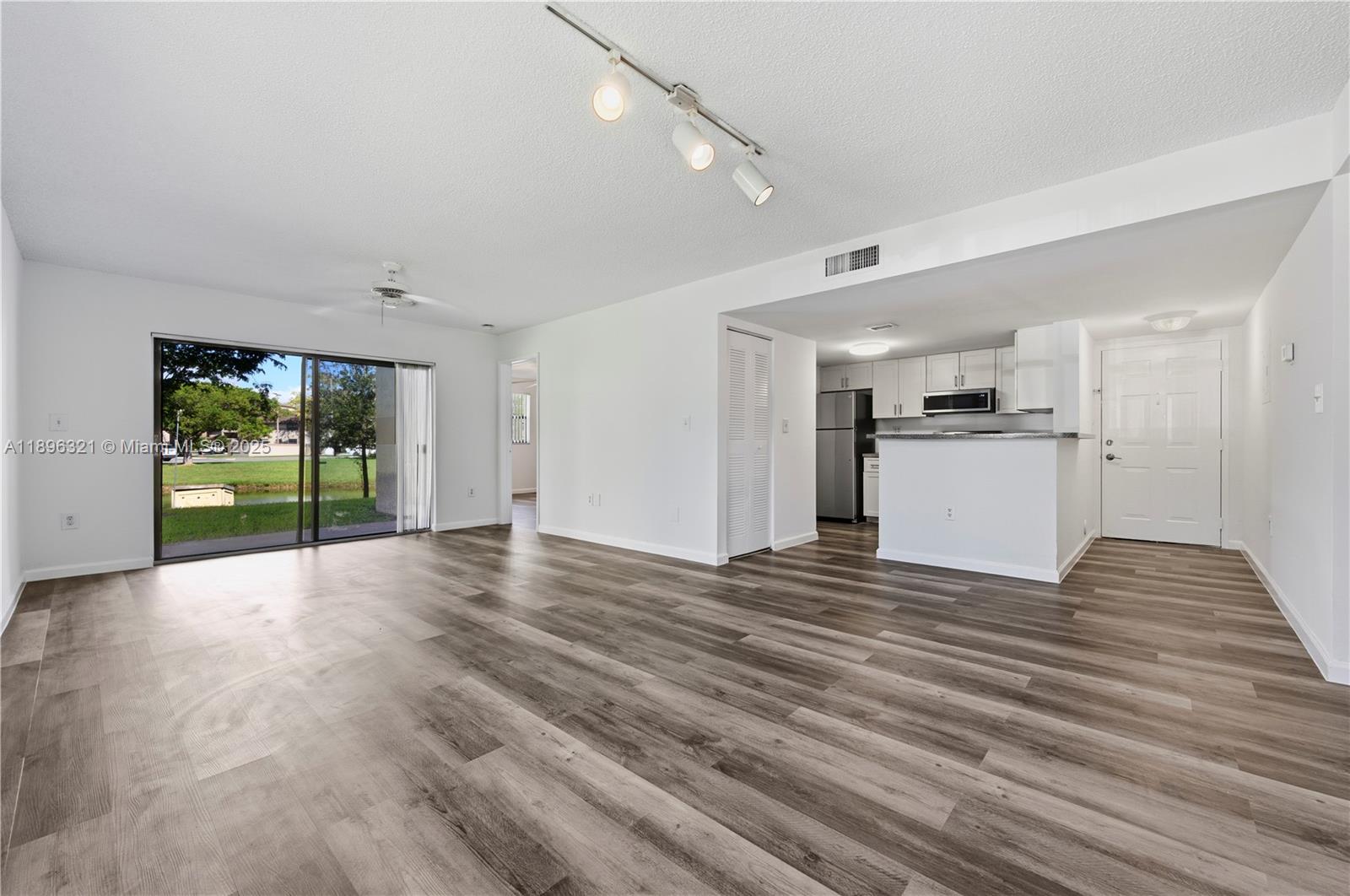 An open-concept living area features wood-look flooring, a kitchen with white cabinets, and sliding doors — 9877 Nob Hill Ct # 9877, Sunrise FL 33351, SUNRISE, FL