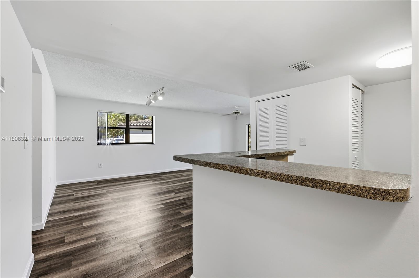 A living area with wood-look flooring, a breakfast bar, and a window with blinds — 9877 Nob Hill Ct # 9877, Sunrise FL 33351, SUNRISE, FL