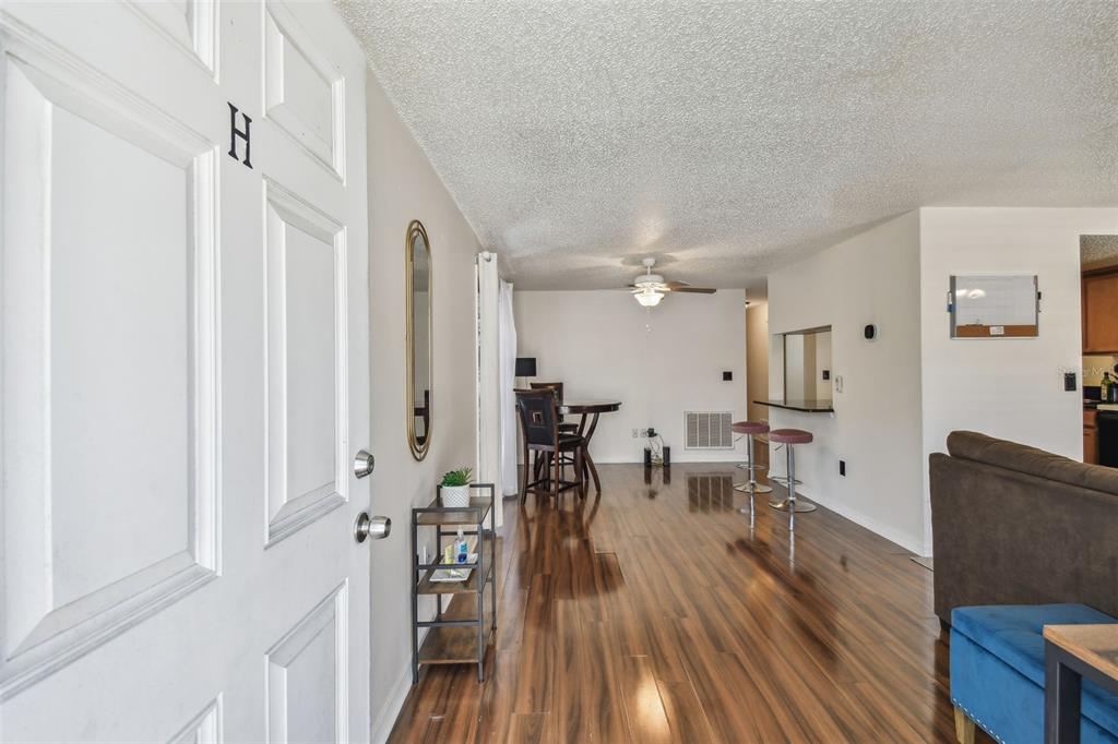 An interior view of an apartment entrance showing wood-look flooring, a dining area, and kitchen — 134 SYCAMORE LANE UNIT H, OLDSMAR, FL