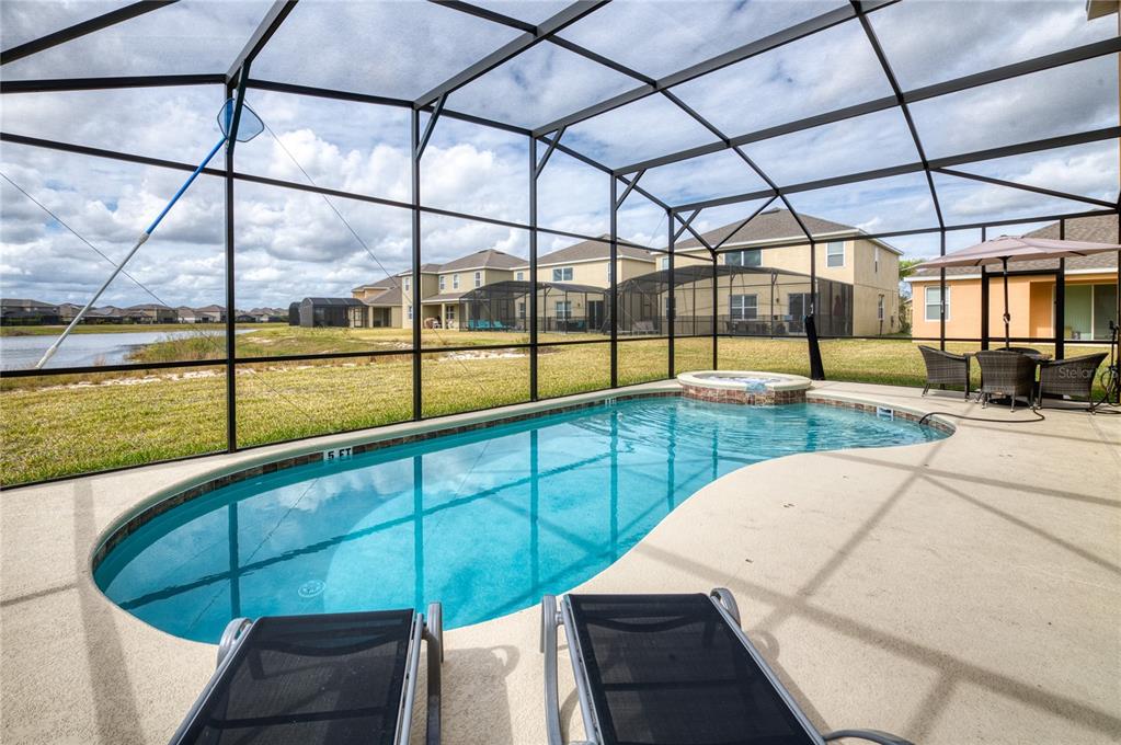 A screened-in pool and hot tub overlook a pond behind a suburban house — 2219 CROFTON SPRINGS COURT, DAVENPORT, FL