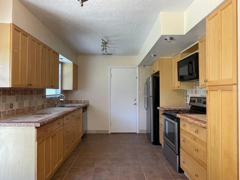 A kitchen features light wood cabinets, tile countertops, stainless steel appliances, and brown floor tiles — 512 GALLOWAY AVENUE, DELTONA, FL