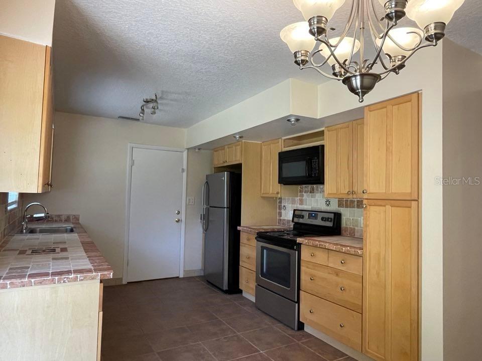 A kitchen features light wood cabinets, stainless steel appliances, and tiled countertops and flooring — 512 GALLOWAY AVENUE, DELTONA, FL