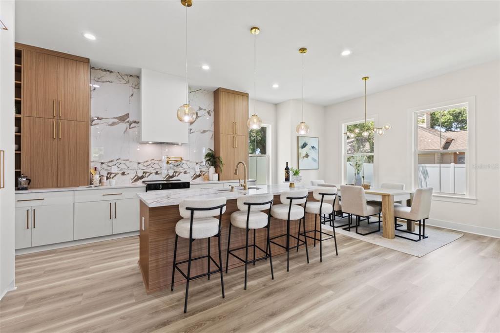 A modern kitchen features wood-toned cabinetry, a marble-topped island with bar seating, and dining area — 10198 HODSON PLACE, SEMINOLE, FL