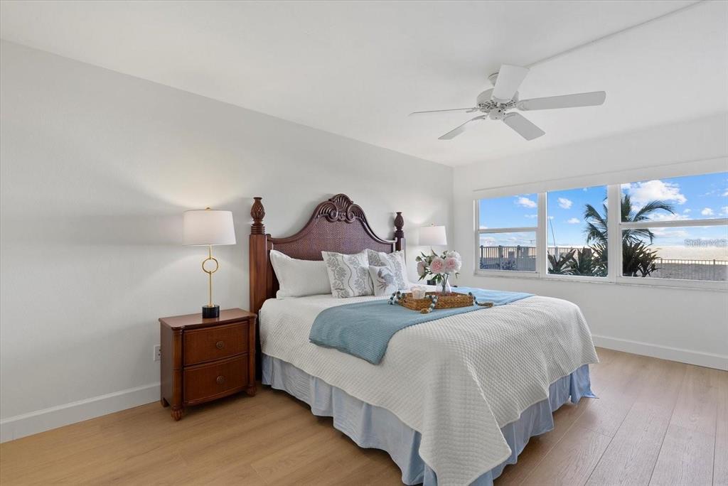 A bedroom features a wooden headboard, light wood flooring, and a window with a beach view — 255 THE ESPLANADE N UNIT 106, VENICE, FL