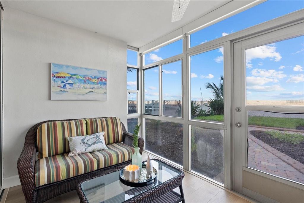 A sunroom features a wicker sofa, a glass coffee table, and large windows overlooking outdoors — 255 THE ESPLANADE N UNIT 106, VENICE, FL