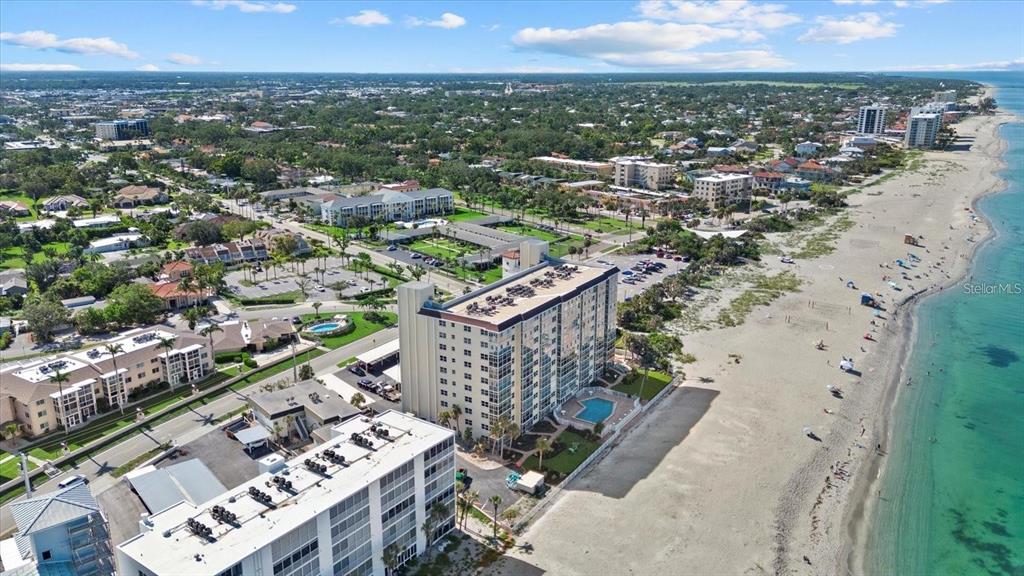 An aerial view shows beachfront high-rise condominiums, a swimming pool, and a sandy coastline — 255 THE ESPLANADE N UNIT 106, VENICE, FL