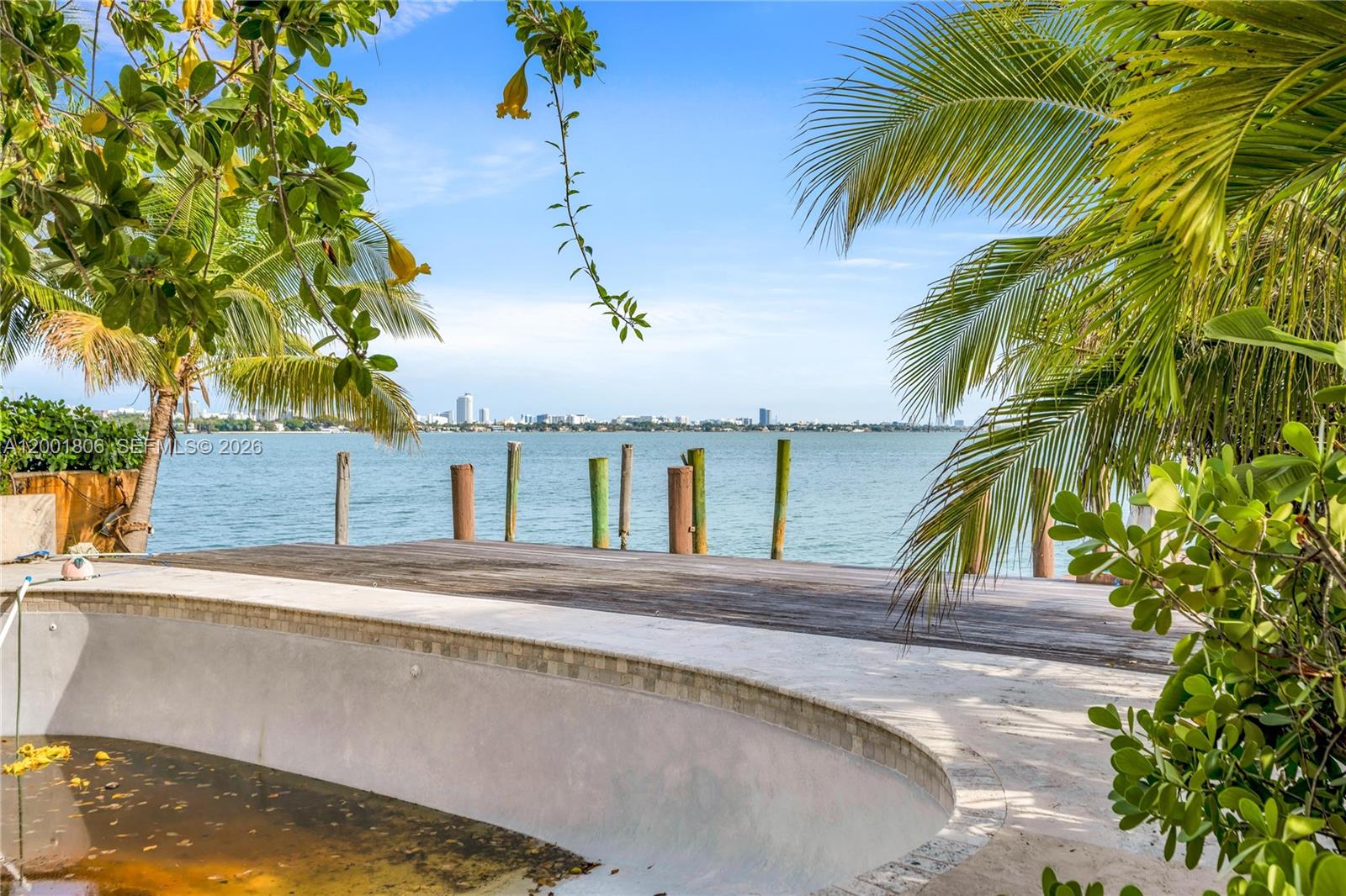 An empty swimming pool sits next to a wooden deck overlooking a bay and skyline — MIAMI BEACH, FL