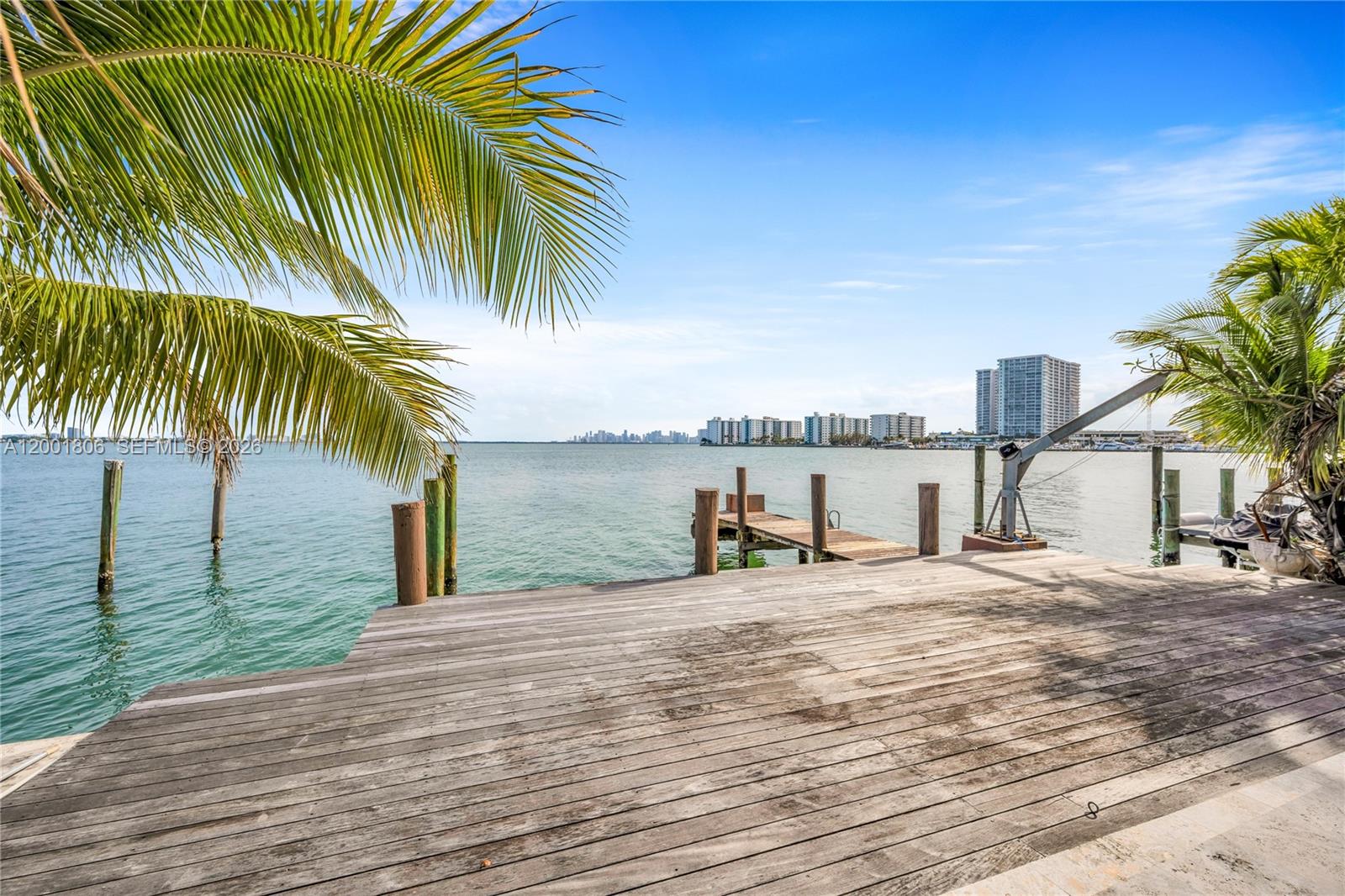A wooden deck overlooks a bay with a small pier and distant city skyline — MIAMI BEACH, FL