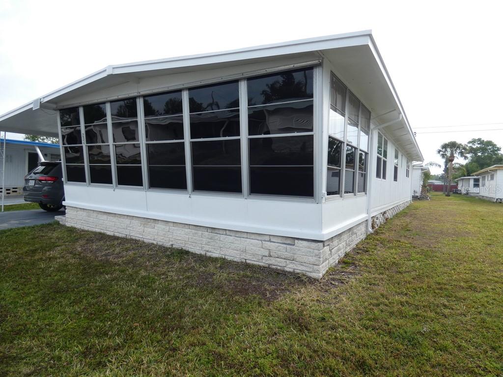 A mobile home exterior features a white enclosed sunroom with large windows and stone skirting — 2900 GULF TO BAY BOULEVARD UNIT 234, CLEARWATER, FL