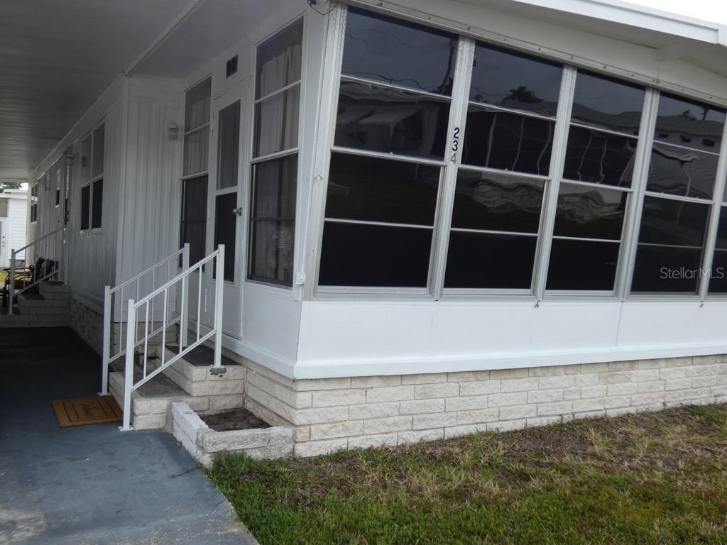 The exterior of a mobile home features a white enclosed porch with stairs and railings — 2900 GULF TO BAY BOULEVARD UNIT 234, CLEARWATER, FL