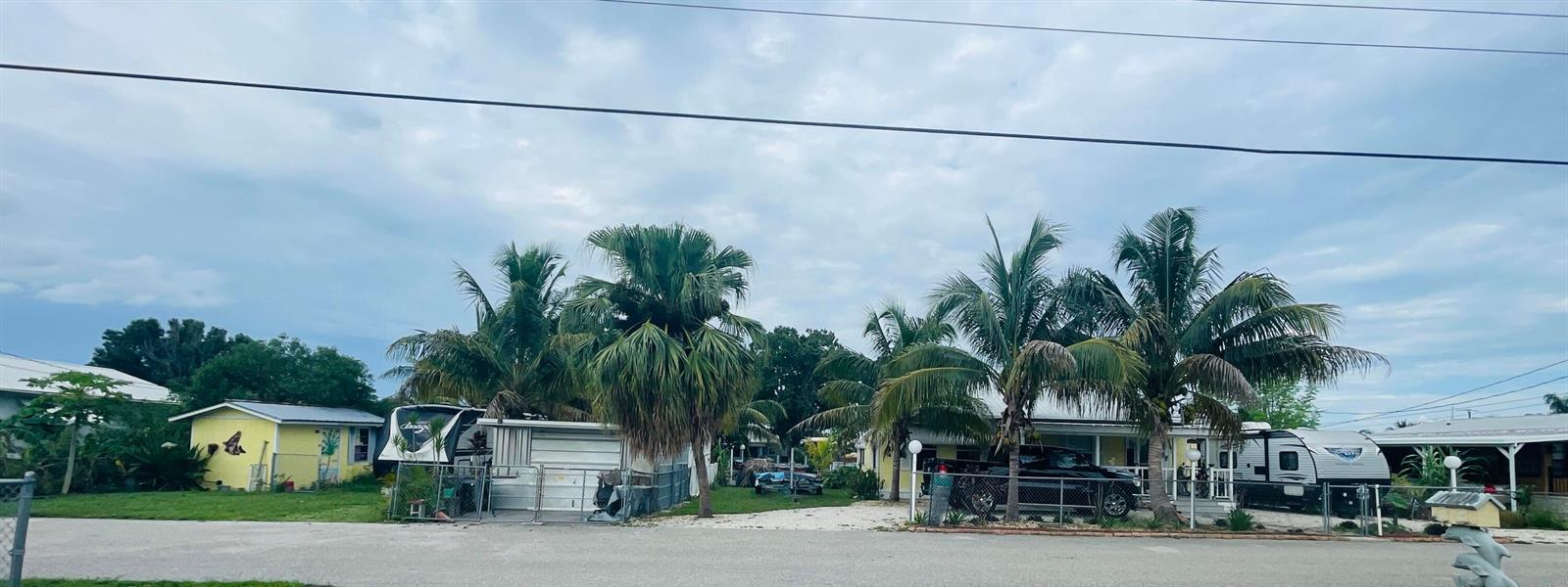 A street view of two small houses with palm trees, a fence, and parked recreational vehicles — 1099 7th Street, Okeechobee FL 34974, OKEECHOBEE, FL