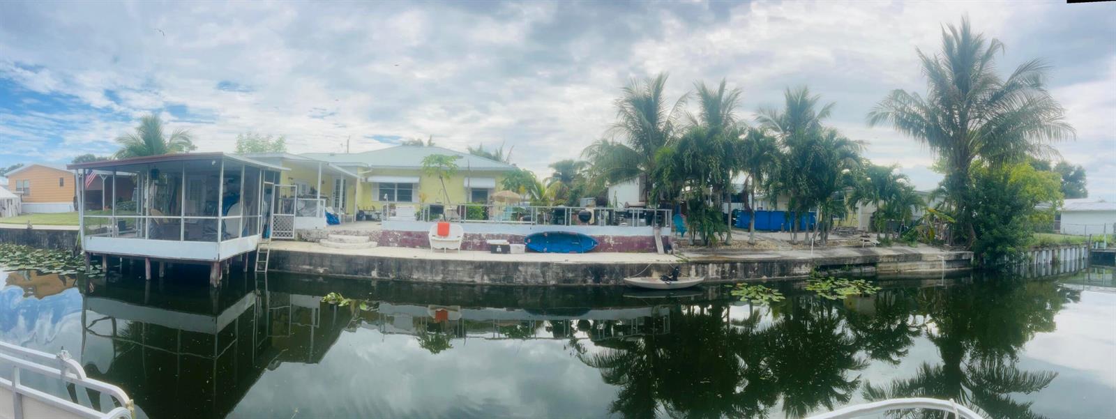 A yellow house with a screened porch sits along a canal with a concrete seawall — 1099 7th Street, Okeechobee FL 34974, OKEECHOBEE, FL