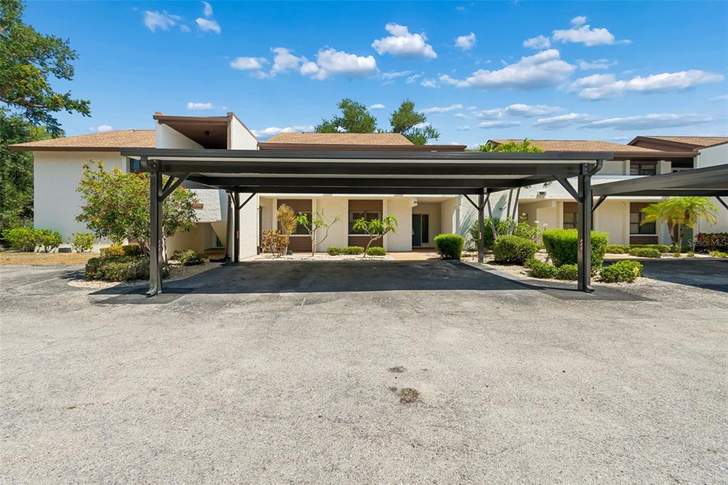 A covered carport sits in front of a two-story residential building with light-colored stucco walls — 6067 FAIRWAY LANE UNIT 1413, BRADENTON, FL