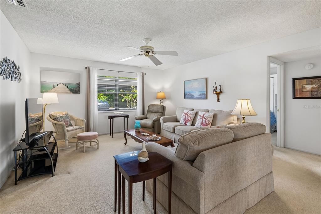 A living room features beige carpet, a ceiling fan, and neutral-toned furniture — 6067 FAIRWAY LANE UNIT 1413, BRADENTON, FL
