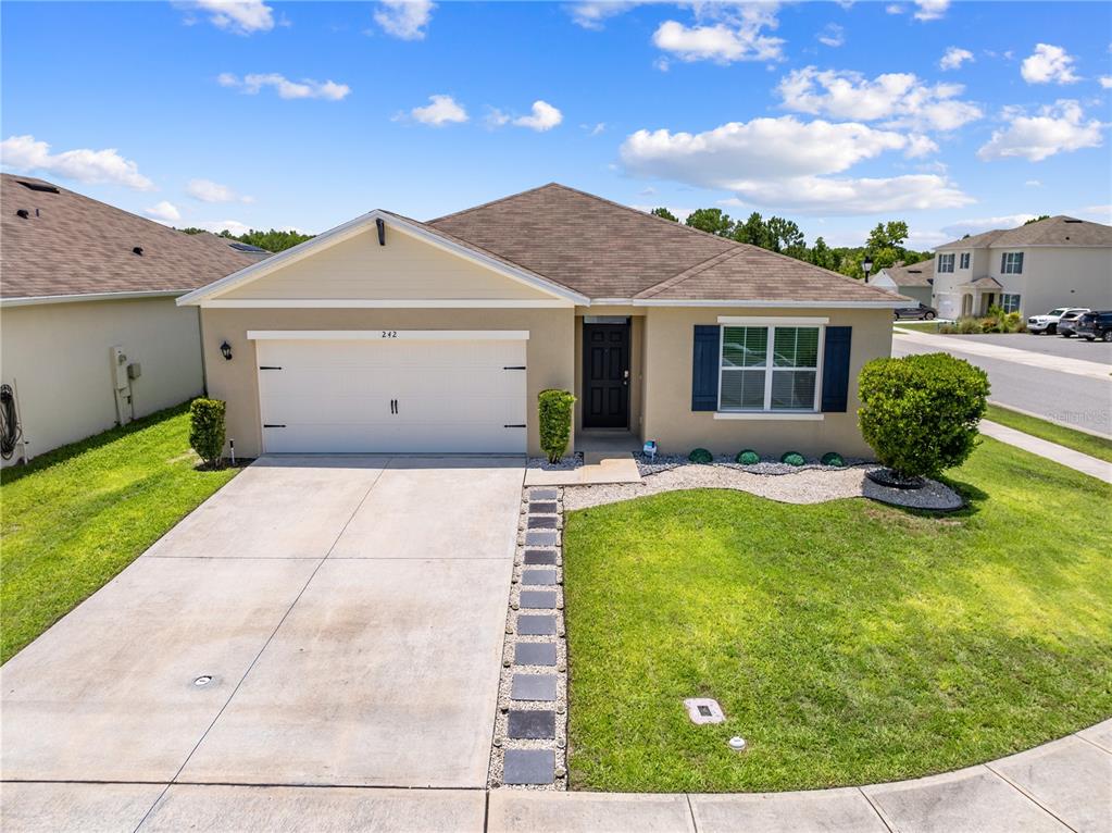 A single-story suburban house with a two-car garage, tan stucco siding, and a paved walkway — 1242 IGUANA LOOP, DAVENPORT, FL