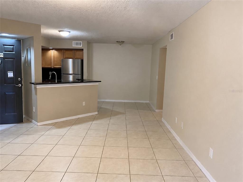 An interior view shows a kitchen with a breakfast bar opening into a tiled living area — 4524 COMMANDER DRIVE UNIT 1615, ORLANDO, FL